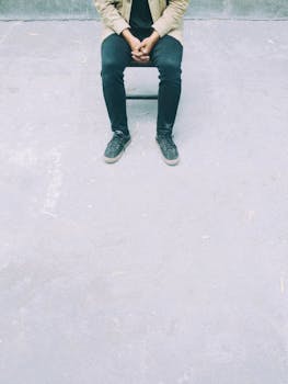 A person sitting casually on a chair against a neutral concrete background.