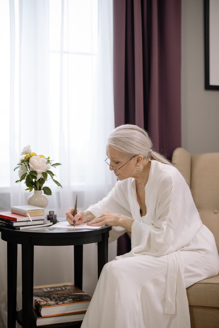 Elderly Woman Sitting On Chair While Writing On A Paper