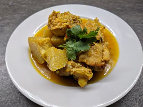 Close-up of a chicken stew dish garnished with fresh herbs on a ceramic plate.