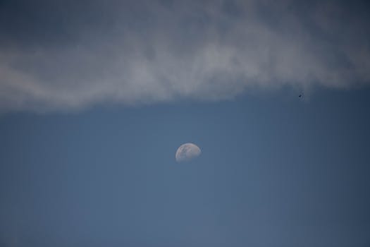 Half moon visible in a clear blue sky with clouds drifting by.