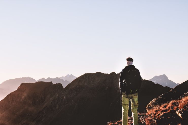 A lone hiker standing on a mountain summit looking out over the horizon, representing the planetary mission and big-picture direction of a Destiny Matrix life purpose
