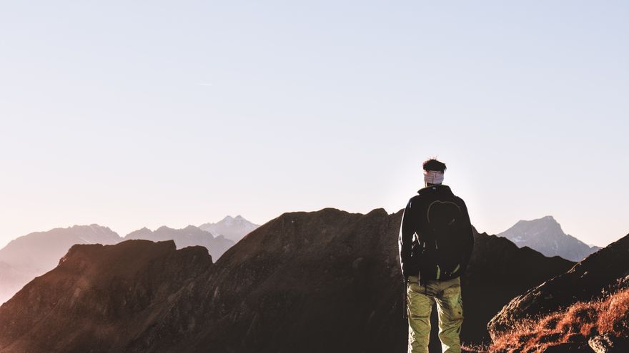 A lone hiker standing on a mountain summit looking out over the horizon, representing the planetary mission and big-picture direction of a Destiny Matrix life purpose