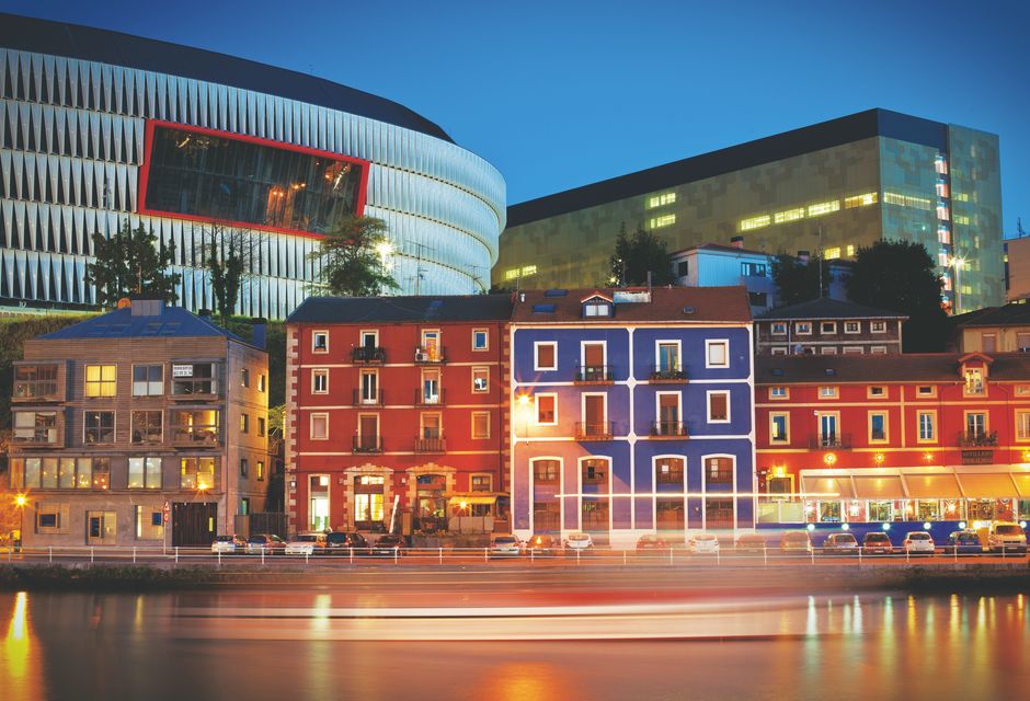 Colorful riverside buildings and San Mamés Stadium in Bilbao illuminated against the night sky. — Photo by Aritz Jauregui on Pexels