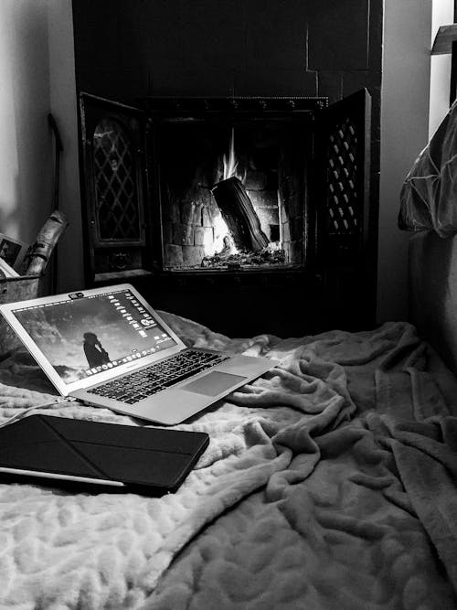Free Black and white of modern netbook with tablet on bed with soft blanket in cozy bedroom with burning firewood at home Stock Photo