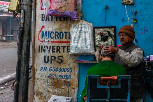 A street barber performing a haircut outside a shop in Delhi, India.
