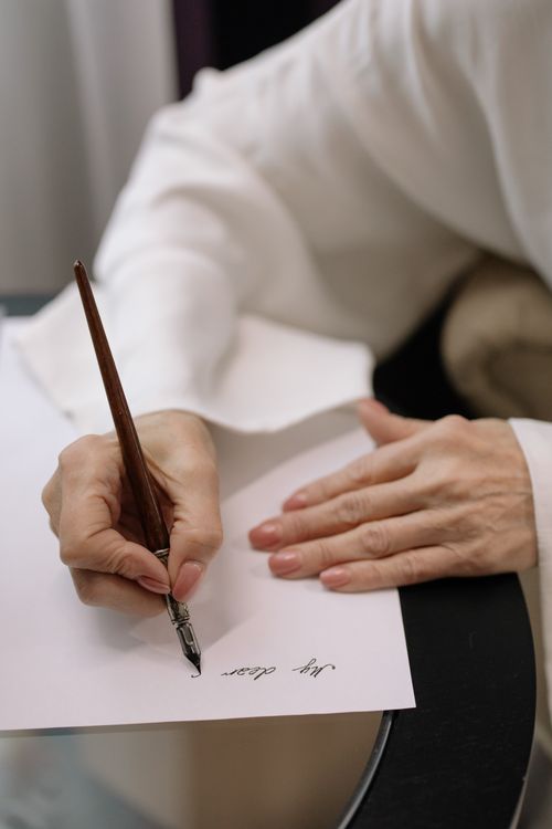 Free Elegant close-up shot of hands writing a letter using a fountain pen on paper. Stock Photo