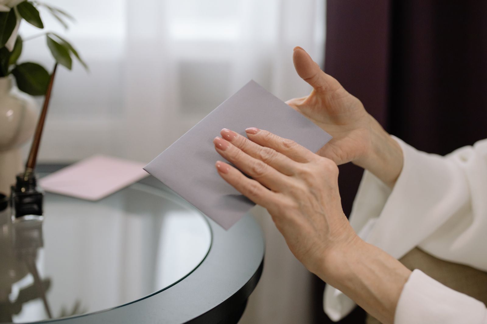 Hands sliding a letter into a pale envelope beside a round glass table