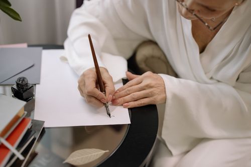 Free Close-up of a person writing with a fountain pen on white paper at a glass table. Stock Photo