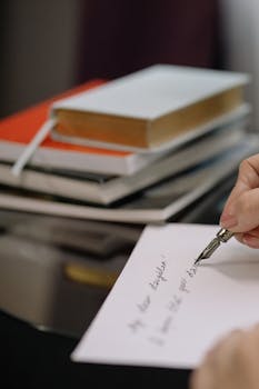 Close-up of a hand writing with a fountain pen beside a stack of books, creating an intellectual ambiance.
