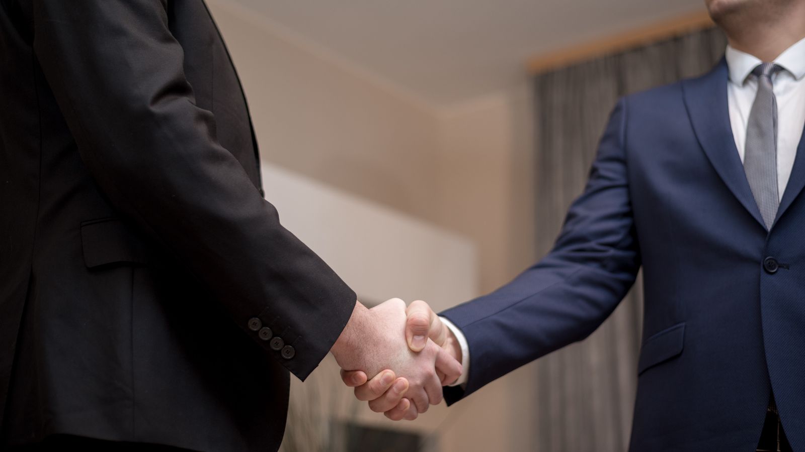 Two businessmen in suits shaking hands, emphasizing trust and partnership indoors.