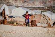 Ethnic girl standing near refugee tents