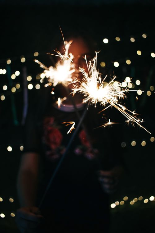 Free A woman enjoys a night scene holding sparklers, surrounded by bokeh lights and a dark background. Stock Photo