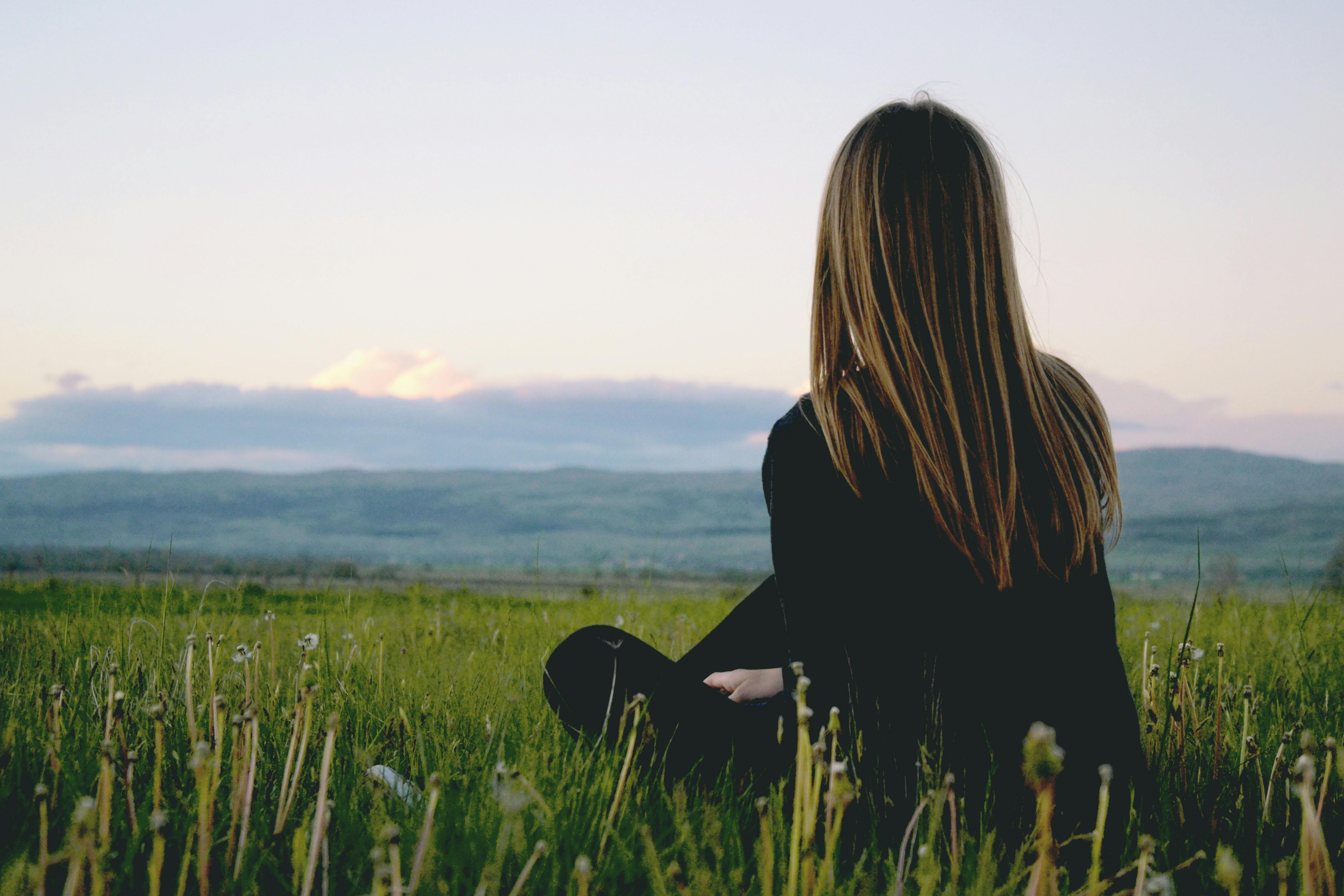 A teenage girl sitting on the green grass field. | Photo: Pexels