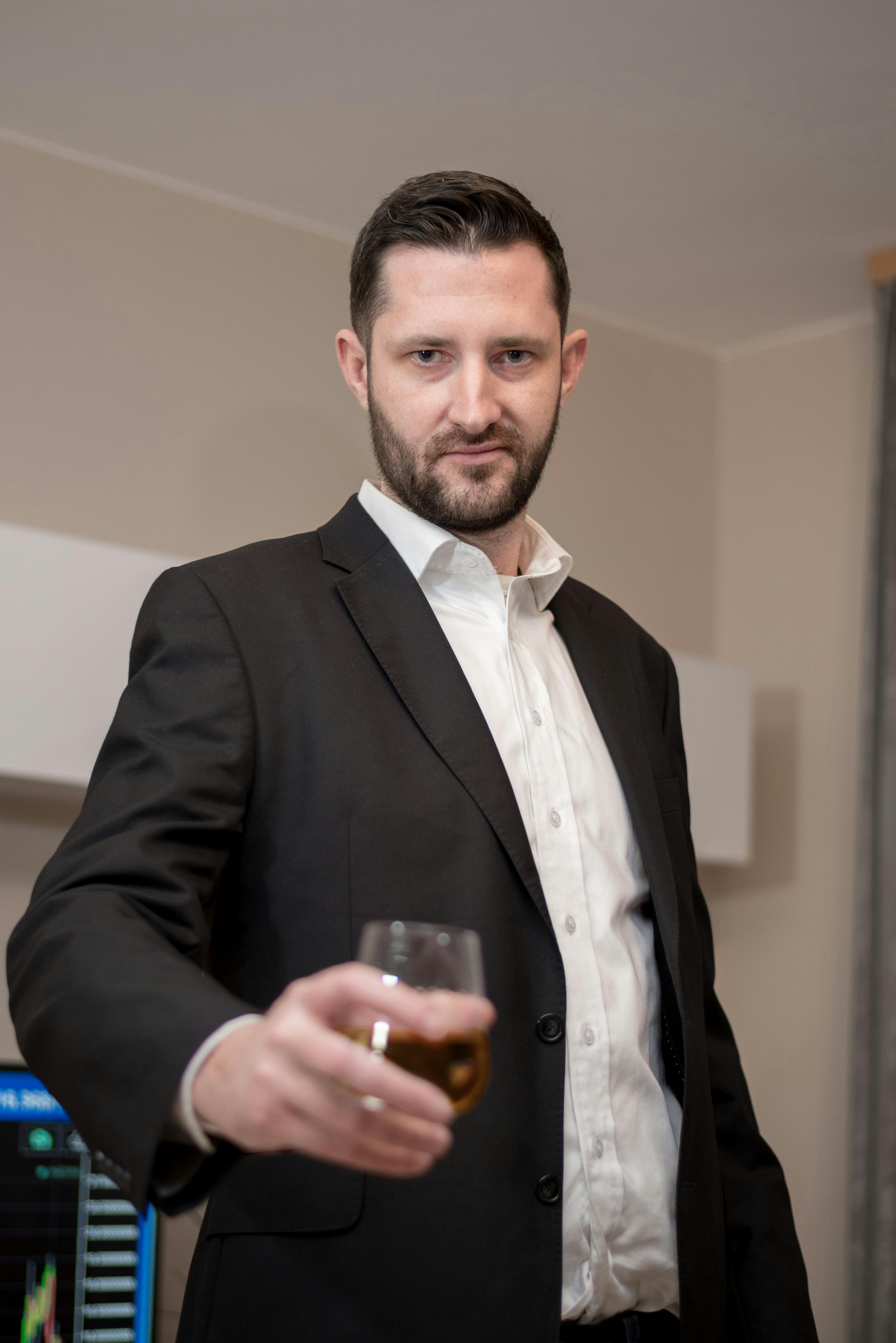 A confident businessman in a suit holding a glass of whiskey indoors.