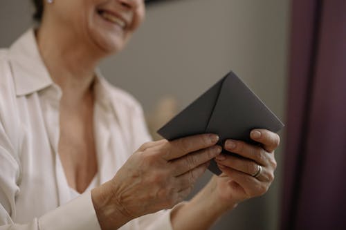 Free A close-up of a smiling senior woman holding an envelope indoors on a sunny day. Stock Photo