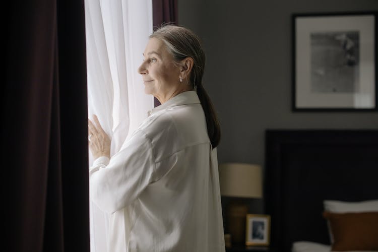 Elderly Woman Standing In Front Of A Window