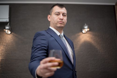 Free A businessman in corporate attire offers a glass of whiskey in an indoor setting. Stock Photo