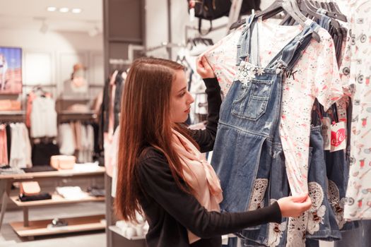 A young woman browses clothing in a fashionable boutique, examining a denim dress.