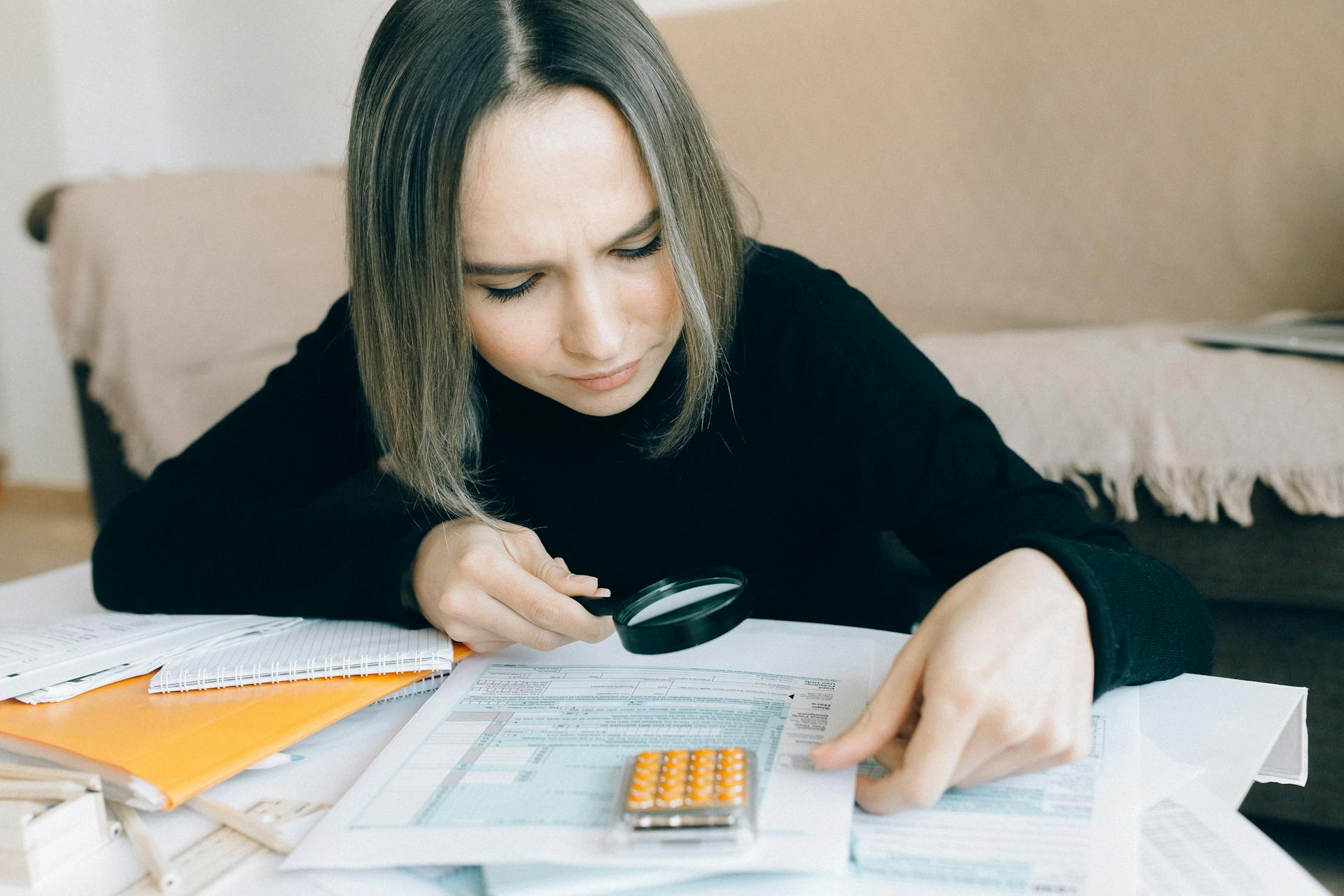 A focused young woman examines documents with a magnifying glass, highlighting attention to detail in accounting tasks.