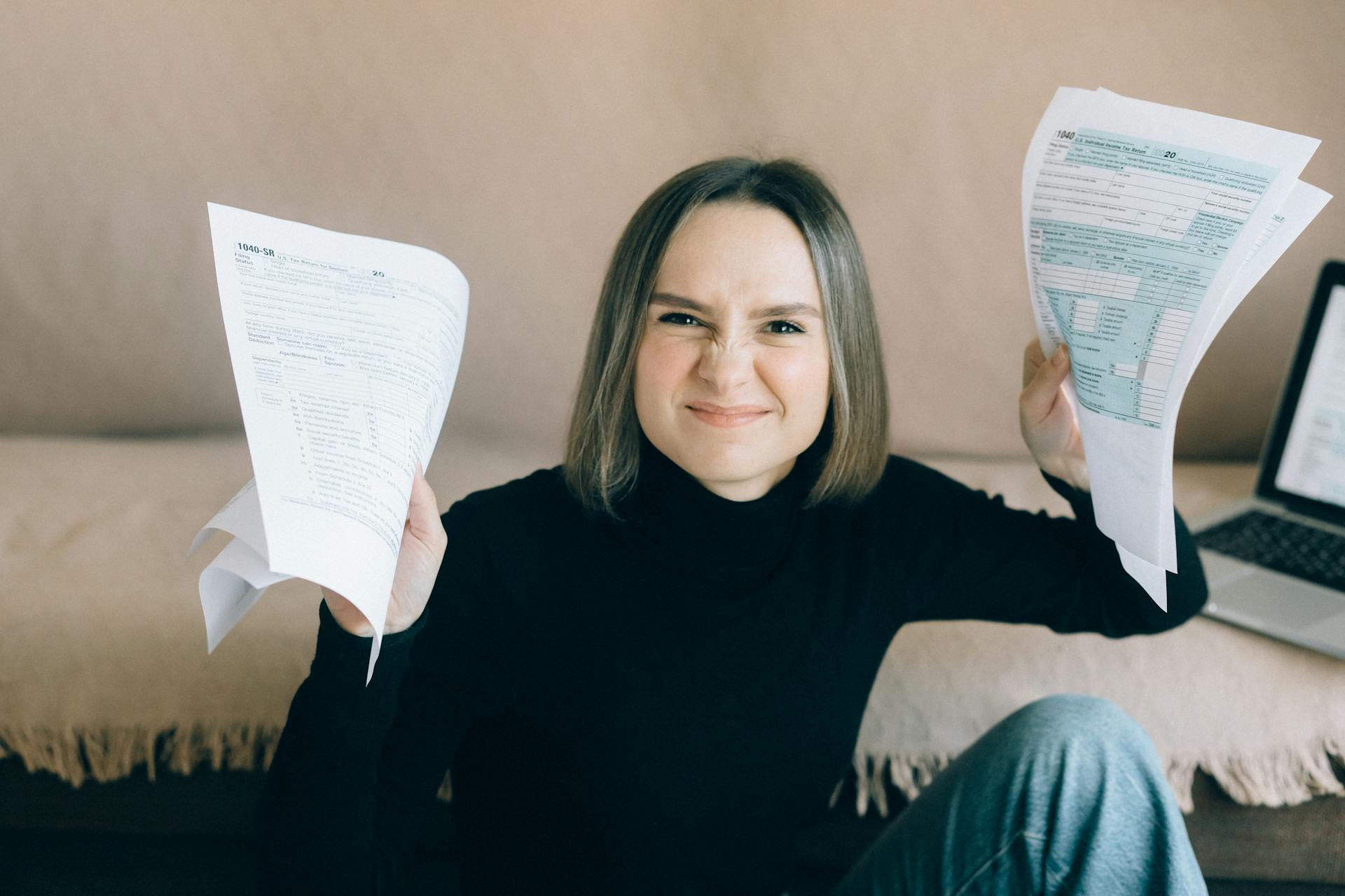 Frustrated young woman holding tax documents while sitting indoors.