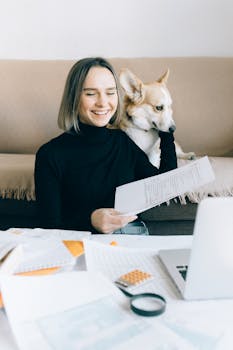 Woman working from home with her pet dog, papers and a laptop on the table.