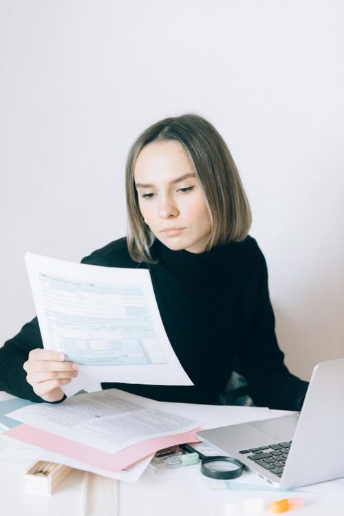 Free Focused woman reviewing paperwork at her desk with a laptop, showcasing a professional working environment. Stock Photo