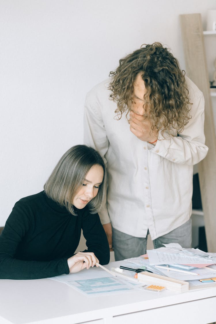 A Man And Woman Having Conversation While Looking At The Papers On The Table