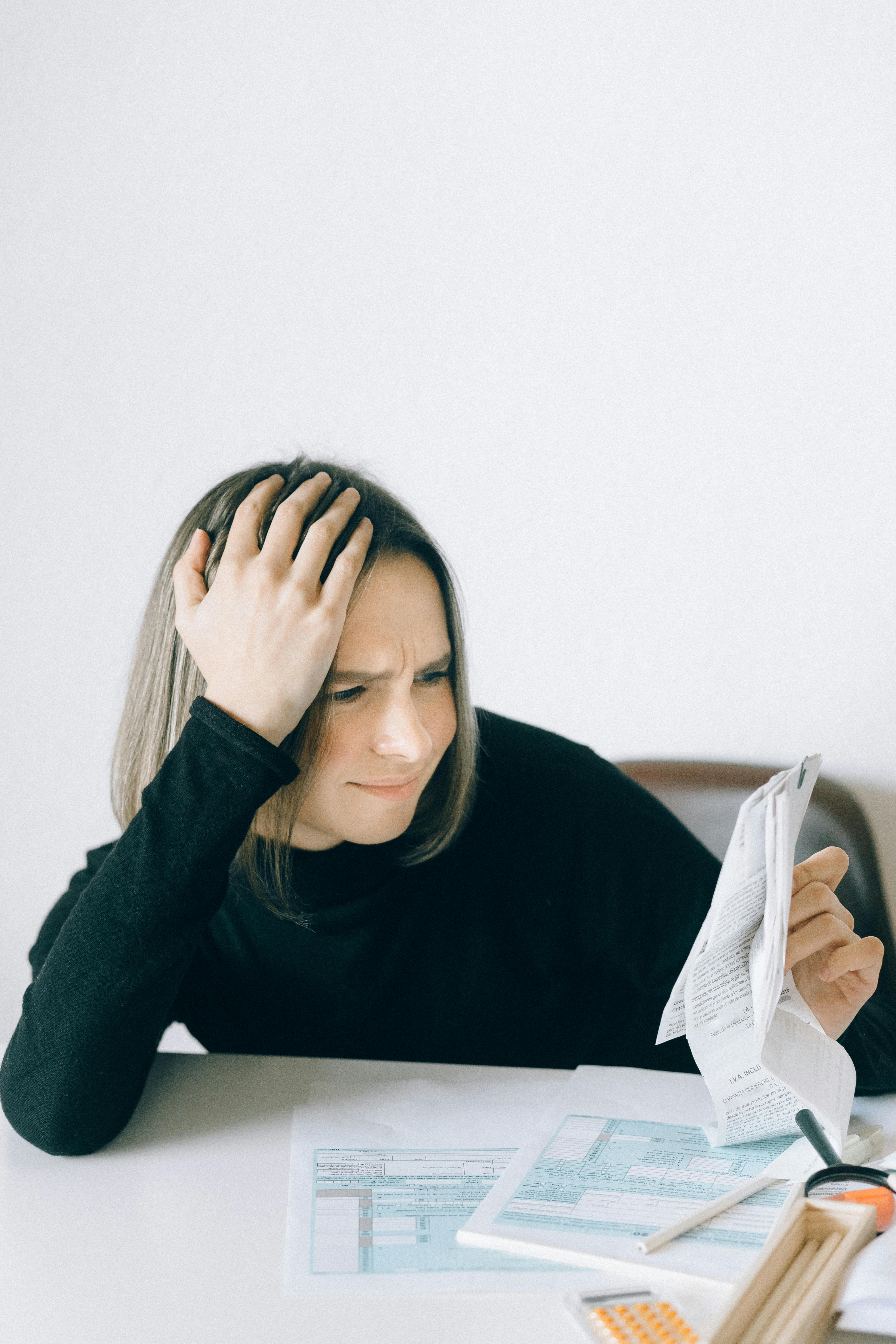 a woman in black long sleeves holding papers with her hand on her head