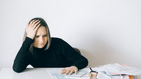 Woman in black sweater stressed with financial paperwork, overwhelmed at white table.
