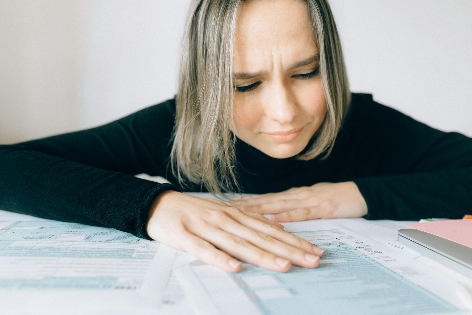 A worried woman analyzing financial paperwork at her desk, signifying stress during tax season.