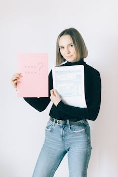 Woman in turtleneck holding tax forms and a pink question sheet indoors.