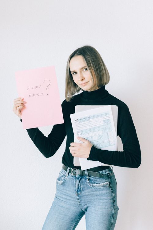 Free A woman in a black turtleneck holding tax forms and a pink paper, standing against a white background. Stock Photo