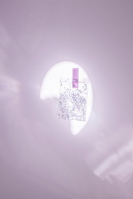 A translucent bag with glitter taped to a purple wall, creating a whimsical and artistic display.