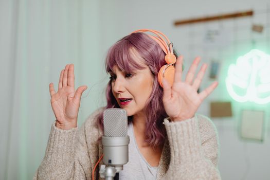 A woman podcasting in a studio setting with a microphone and headphones, gesturing expressively.