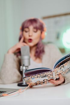Female podcaster with headphones reads a book into a microphone.