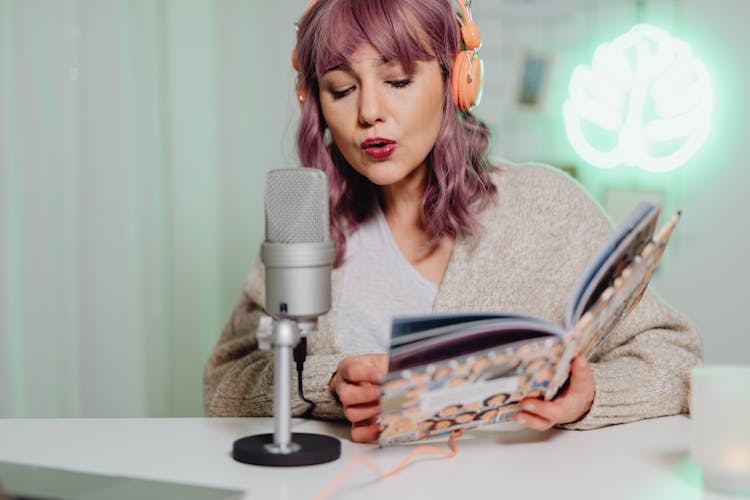 A Woman Talking On A Microphone While Reading A Book