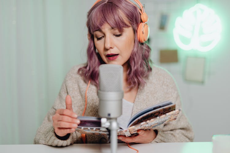 A Woman Talking On A Microphone While Reading A Book