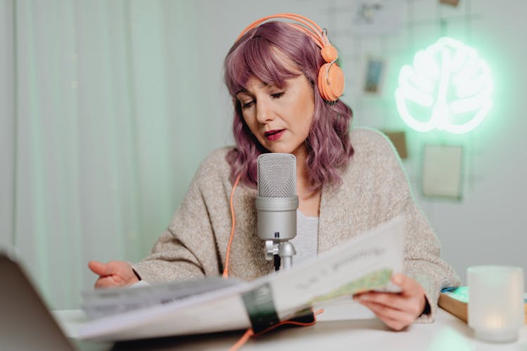 A Woman Talking On A Microphone While Reading A Book