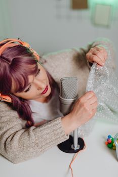 Woman using bubble wrap and microphone for ASMR content with Canon EOS.