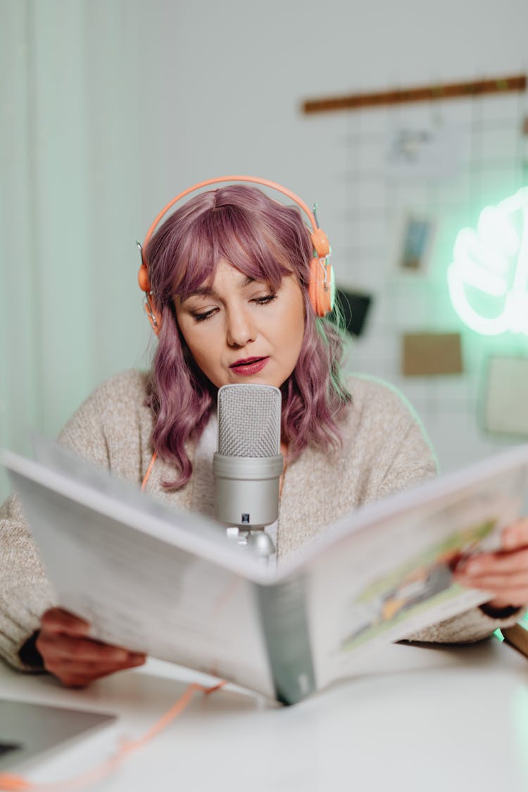 
A Woman Talking On A Microphone While Reading A Book