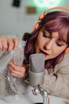 Young woman with purple hair using bubble wrap and microphone for ASMR video.