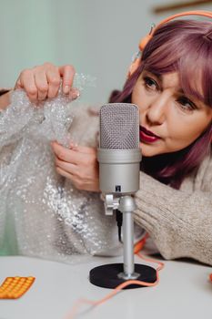 Woman with purple hair using microphone and bubble wrap for ASMR recording in studio setting.