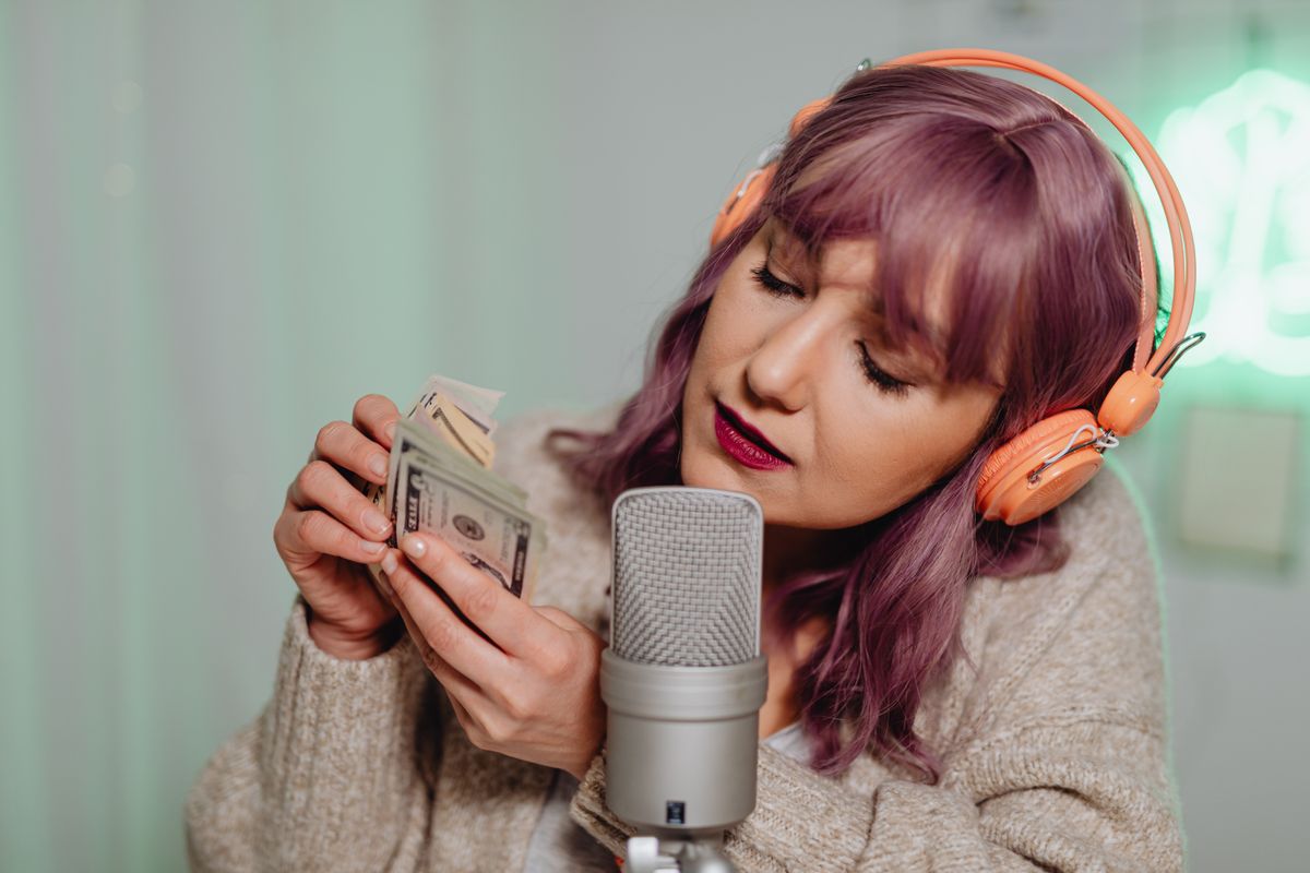 Woman wearing headphones recording ASMR with cash and microphone indoors.