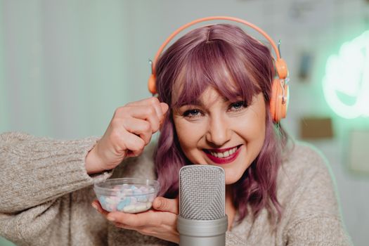 Woman with purple hair performing ASMR with candy and microphone indoors.