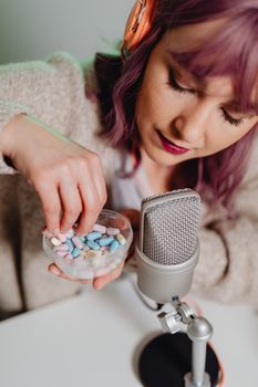 Woman with purple hair creating ASMR video using colorful candies and microphone.