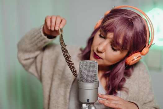 A woman uses a feather and microphone for ASMR recording in a cozy home studio.