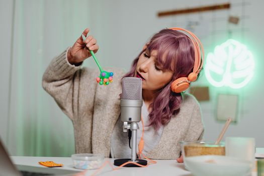 A woman with colored hair engaged in ASMR, using microphone and toy.