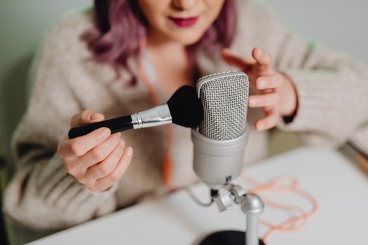 A woman records ASMR content with a microphone and brush, focusing on sound details.