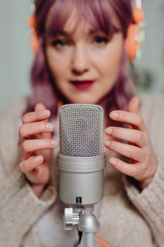 Woman with headphones recording ASMR using a microphone, focusing on sound quality.