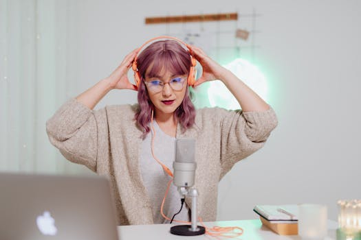 A young woman wearing headphones records a podcast in a stylish home studio.